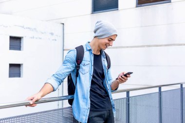 Şehir tarzı bir adam cep telefonu kullanarak duvarın yanında duruyor.