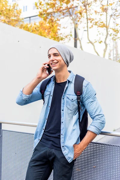 Urban stylish man standing by the wall using cellphone