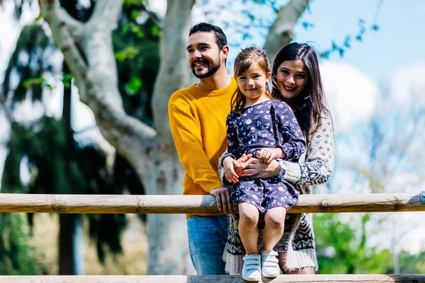 Küçük kız kameraya bakarken mutlu aile yeşil parkta duruyor.