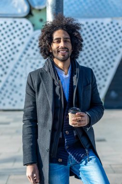 Genç Afrikalı Amerikalı adam mutlu gülümsüyor. Yüzünde gülümsemeyle kasaba sokaklarında kahve içerek..