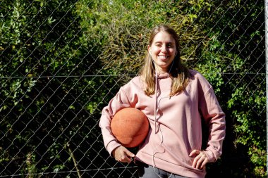 Genç, uzun saçlı, elinde basket topu tutan kız.