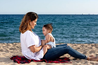 Gülümseyen anne plaj havlusunda yeni doğmuş bebekle oynuyor.