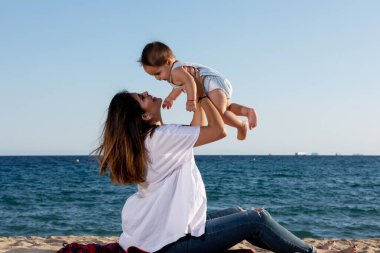 Gülümseyen anne plaj havlusunda yeni doğmuş bebekle oynuyor.