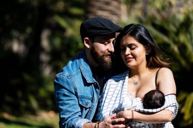 Mutlu çift yeni doğan bebeklerini kollarında tutuyor. Açık havada.