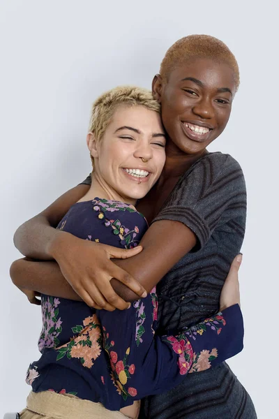 Neşeli bayanların fotoğrafı, beyaz arka planda soyutlanmış, farklı ırktan, sıradan kazaklar giymiş, birlikte olmaktan zevk alıyor ve kucaklıyor. Çeşitli kadınlar mutlu bir şekilde gülüyor, birlikte eğleniyorlar..