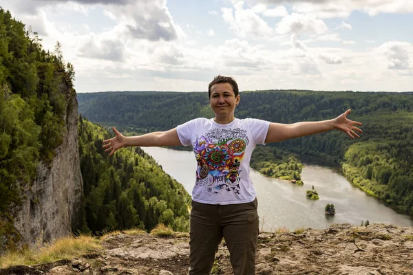 Happy middle-aged woman tourist happy on reaching up top of mountain, standing on edge with arms outstretched on beautiful natural background. Selective focus. Shallow depth of field. Copy space.