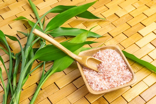 Spa, zen, massage concept. Pink himalayan bath salt with spoon, bamboo leaves, soap in soap dish on wooden carpet background. Top view. Close up. Selective focus. Text copy space.
