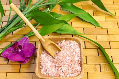 Spa, zen, masaj konsepti. Pembe Himalaya banyo tuzu, kaşık, bambu yaprağı, mor orkide, ahşap halı zemininde sabun kabı. Üst Manzara. Kapatın. Seçici odaklanma. Metin kopyalama alanı.