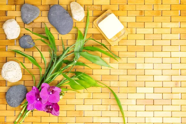 Spa, zen, massage concept. Bamboo leaves, bath soap in soap dish, white black stones, purple orchid on wooden background. Top view. Flat lay. Close up. Selective focus. Copy space.