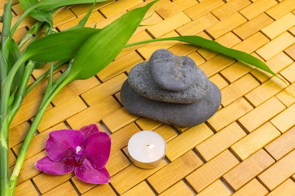 Spa, zen, massage concept. Bamboo leaves, black stones, purple orchid, lighting candle on wooden background. Above view. Close up. Selective focus with copy space