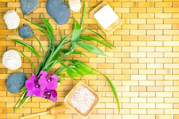 Spa, zen, massage concept. Bath salt, bamboo leaves, soap in soap dish, spoon, white black stones, purple orchid on wooden background. Top view. Flat lay. Close up. Selective focus. Copy space.