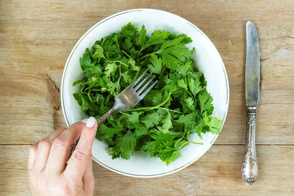 Female hand eating green herbal salad from plateon old wooden table. Healthy eating dieting concept — Stock Photo, Image