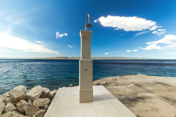 Shower on a rocky beach, blue sea in the background — Stockfoto