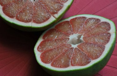Kırmızı arkaplandaki kırmızı çiçek yapraklarının yüzeyi, kırmızı pomelo, yarı yarıya kesilmiş, pomelo eti dokusu.