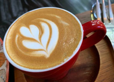 Ahşap tepside bir fincan latte sanatı, güzel köpüklü latte sanatı, kırmızı renkli seramik bardak, şık tonlama. 