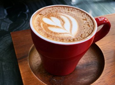 Ahşap tepside bir fincan latte sanatı, güzel köpüklü latte sanatı, kırmızı renkli seramik bardak, şık tonlama. 