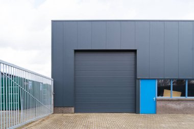 Tekerlekli kapıları ve mavi giriş kapısı olan küçük sanayi deposu.