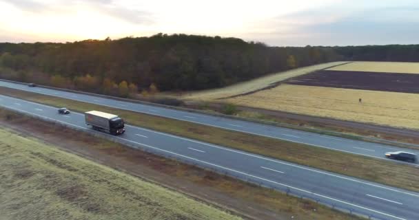 De truck rijdt de zonsondergang tegemoet op een rechte weg. De truck rijdt langs de weg tussen velden bij zonsondergang — Stockvideo