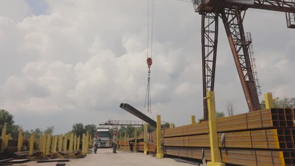 Мостовой кран загружает металл в грузовик, загружает металл на склад, большой мостовой кран, люди работают на металлическом складе — стоковое видео