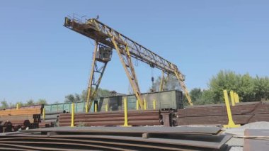 Büyük sarı bir vinç, mavi gökyüzüne karşı metal bir vinçle depoda hareket ediyor.