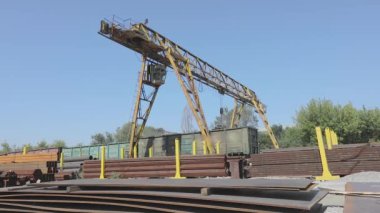 Büyük sarı bir vinç, metal bir vinçle depoda hareket ediyor. Mavi gökyüzüne karşı bir vinç, hızlandırılmış.