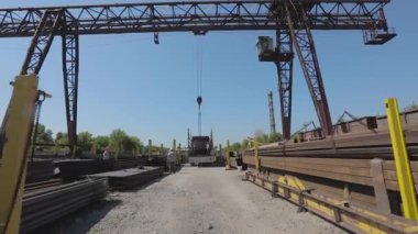 İşçiler bir kamyona metal yükler, insanlar depoda çalışır, kargoyu kamyona yüklerler. Kamyon vincin altında.