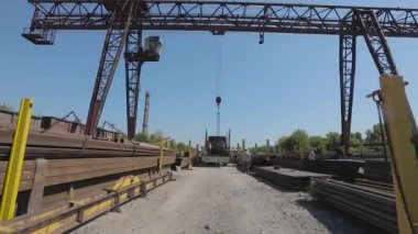 İşçiler bir kamyona metal yükler, insanlar depoda çalışır, kargoyu kamyona yüklerler. Kamyon vincin altında.