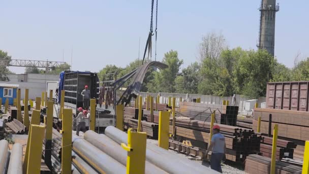 Le processus de travail dans un entrepôt avec un métal. Les travailleurs déchargent un métal dans un camion debout sous une grue portique, les travailleurs sur une rampe. Chargement d'un camion avec une grue portique — Video