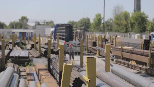 El proceso de trabajo en un almacén con un metal. Los trabajadores descargan un metal en un camión parado debajo de una grúa pórtico, los trabajadores en una rampa. Cargando un camión con una grúa pórtico — Vídeo de stock