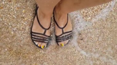 Su, dişilerin ayaklarını yakından yıkar. Deniz dalgalarında dişi bacaklar. Ayaklar deniz suyunda, yakın plan.