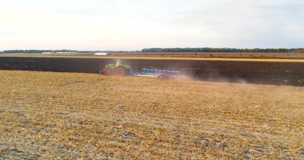 De trekker werkt in het veld. Een veld aan het ploegen met een tractor die van een drone schiet. Drone schieten van een tractor werken in het veld — Stockvideo