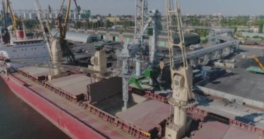 İskele vinci kargoyu kuru bir kargo gemisine yüklüyor. Limanda kuru kargo gemisi var..