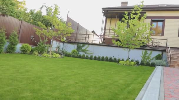 Panorama de una parcela de casa de campo con hermosas plantas y un césped. Hermoso patio trasero con césped y plantas ornamentales — Vídeo de stock