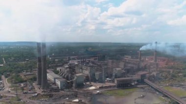 Dumanı tüten bacası olan büyük bir metal bitkinin üzerinden uçmak. Fabrikanın bacasından duman salınımı. Fabrika insansız hava aracı görüntüsünün bacasından yoğun duman çıkıyor.