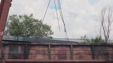 Profil borusunun yükünü yük vagonundan bir vinç boşaltmış. Depoya metal yüklemiş. Büyük bir vinç.