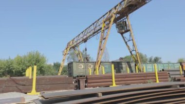 Büyük sarı bir vinç, mavi gökyüzüne karşı metal bir vinçle depoda hareket ediyor.