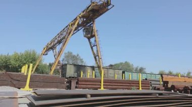 Büyük sarı bir vinç, mavi gökyüzüne karşı metal bir vinçle depoda hareket ediyor.