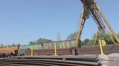 Büyük sarı bir vinç, mavi gökyüzüne karşı metal bir vinçle depoda hareket ediyor.