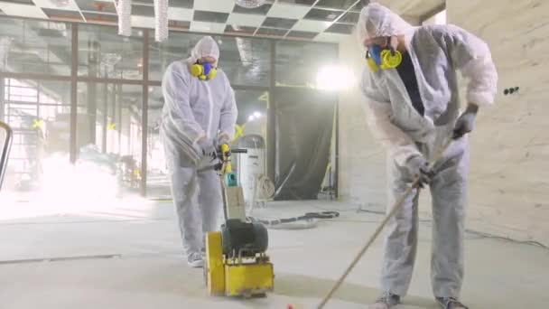 Proceso de trabajo en una obra. Los trabajadores en trajes de protección están moliendo el suelo de hormigón. Profesionales de construcción. Los trabajadores hacen piso de hormigón — Vídeos de Stock