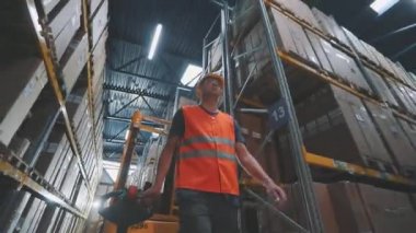 Bir işçi hidrolik forkliftle yük taşır. Büyük, modern bir depo. Stokta modern özel ekipman
