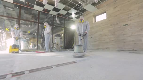 Construction professionals. Working process at a construction site. Workers in protective suits are grinding the concrete floor. Workers make concrete floor — Stock Video