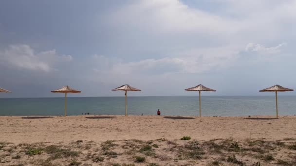 Strandparaplyer på en tom strand storm moln i bakgrunden. Blå moln långt ut i havet. Halmparaplyer på stranden — Stockvideo