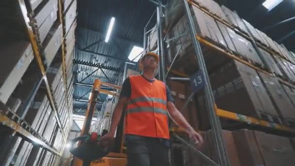 Un lavoratore trasporta un carico su un carrello elevatore idraulico elettrico. Grande magazzino moderno. Attrezzature speciali moderne in magazzino — Video Stock
