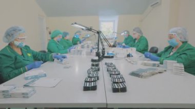 Fabrika işçileri hap taşıyor. Maskeli işçiler. Bir ilaç fabrikasında iş akışı