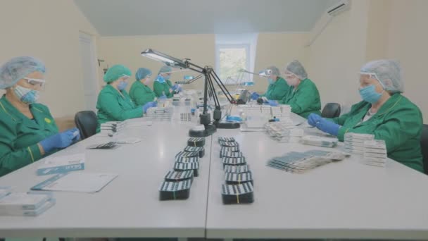 Ženy balí pilulky do balíčku. Dělníci z továrny nosí masky. práce během pandemie — Stock video
