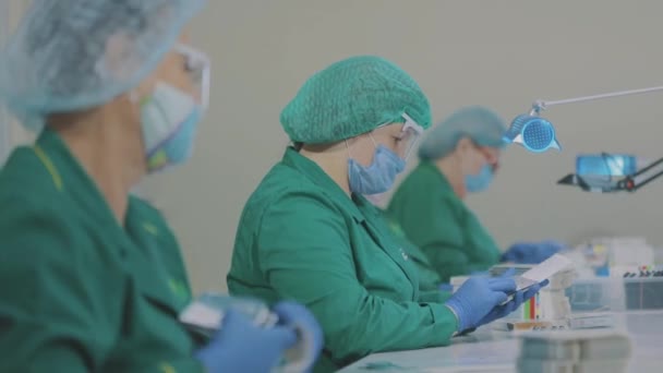 Vrouwen verpakken pillen in een pakje. Fabrieksarbeiders dragen maskers. werk tijdens een pandemie — Stockvideo