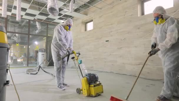 Workers in protective suits are grinding the concrete floor. Working process at a construction site. Construction professionals. Workers make concrete floor — Stock Video