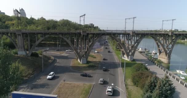 Samochody jadą wzdłuż drogi w mieście widok z góry. Samochody przejeżdżają pod mostem. Wiele samochodów na drodze przejeżdżających pod mostem widok z góry. Ruch samochodowy. — Wideo stockowe