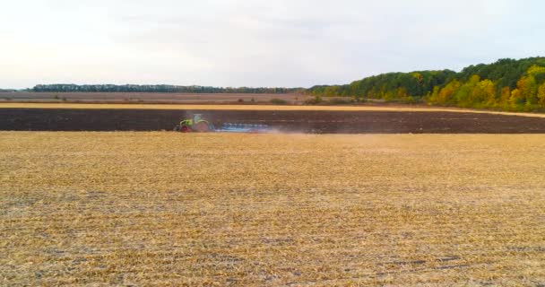 A traktor terepen dolgozik. Egy terepen dolgozó traktor felett repülni. A traktor felszántja a terepet. Repülj át a mezőn egy traktorral — Stock videók