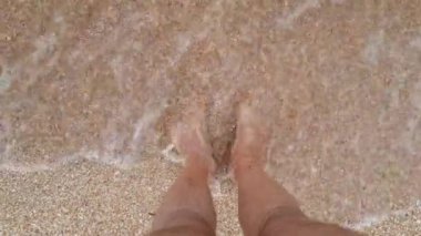 Su insanın ayaklarını yıkar. Deniz dalgalarında erkek ayakları. Ayaklar deniz suyunda, yakın plan.